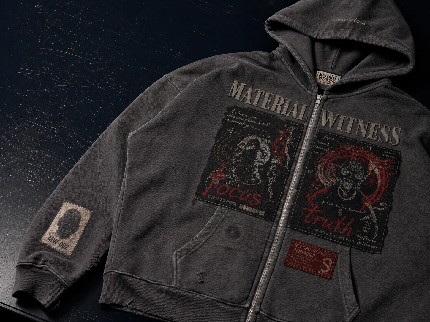 MW–002 washed charcoal patch hoodie documented on a dark worktable